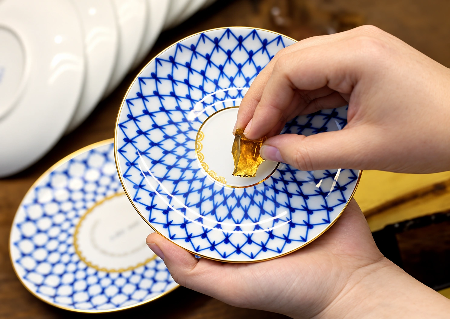 Artisan applying gold decoration to a Cobalt Net porcelain saucer
